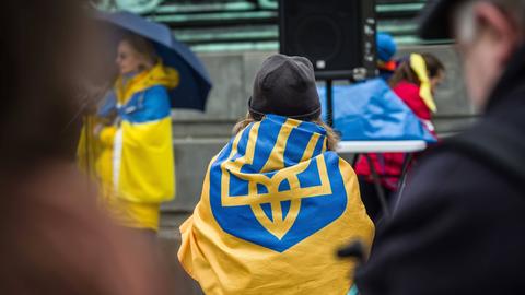 Bei einer Demonstration in München sitzt eine Frau auf der Straße und hat die ukrainische Flagge um sich geschlungen.