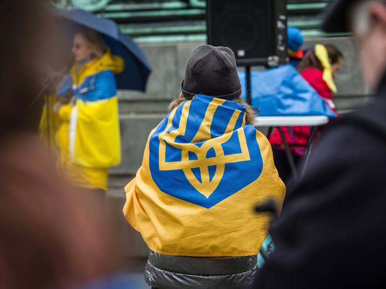 Bei einer Demonstration in München sitzt eine Frau auf der Straße und hat die ukrainische Flagge um sich geschlungen.