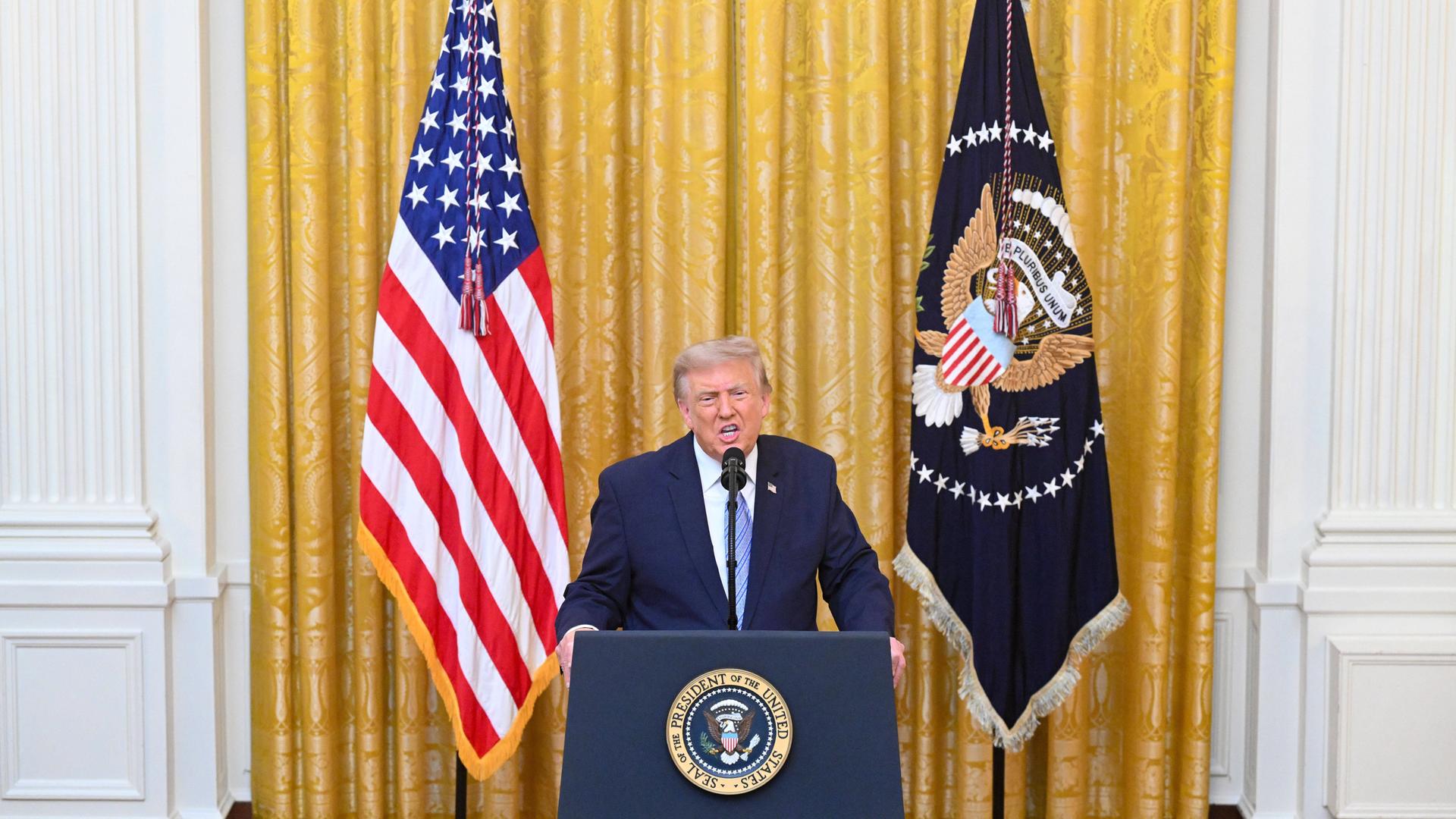 US-Präsident Trump steht bei einer Ansprache an einem Rednerpult zwischen zwei Fahnen.