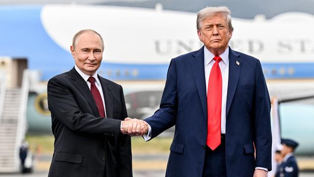 US-Präsident Trump macht einen Hand-Schlag mit Präsident Putin aus Russland. Beide Männer stehen nebeneinander und schauen in Richtung der Kamera.