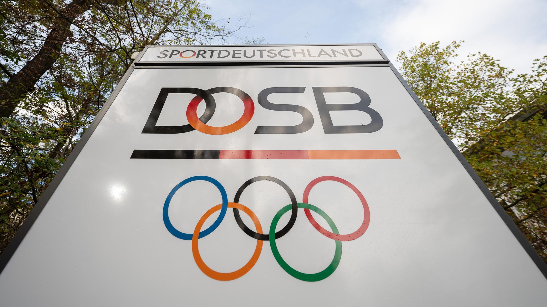 Das Logo "Deutscher Olympischer Sportbund" (DOSB) steht an dessen Hauptsitz auf einem Schild. Die Olympischen Ringe und  der Schriftzug "Sportdeutschland" sind auch abgebildet.