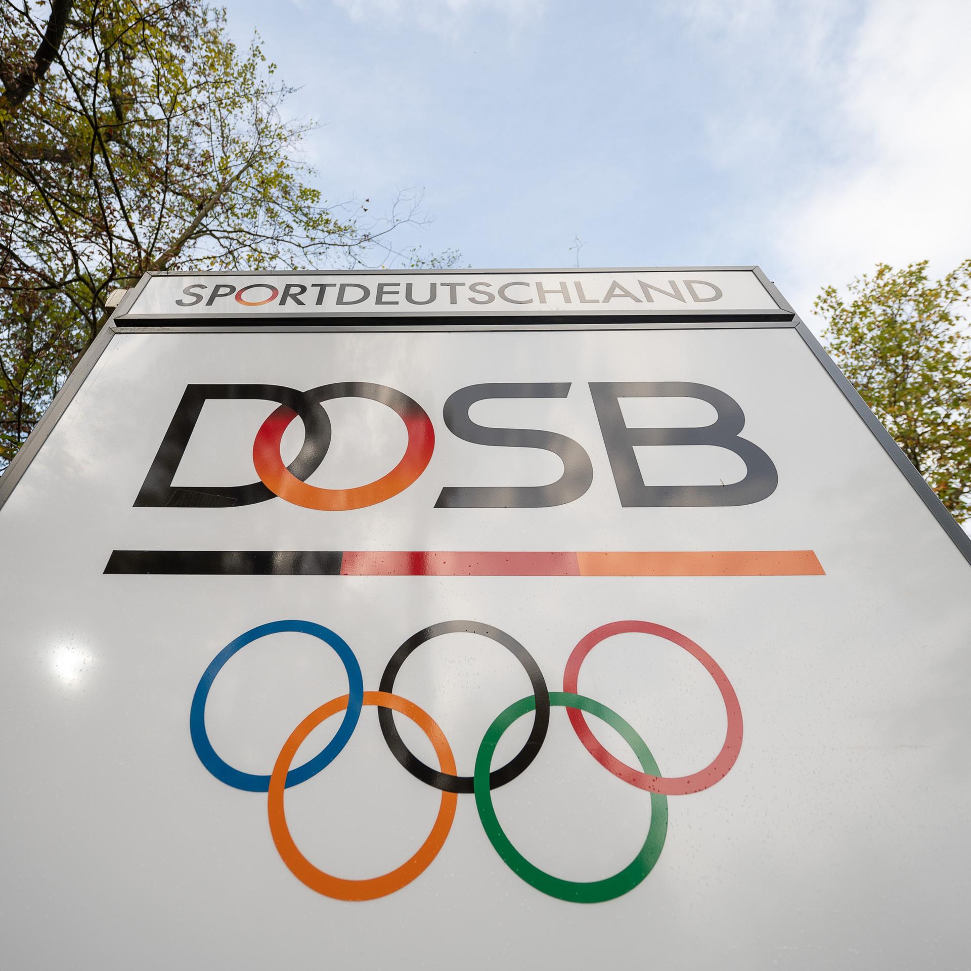 Das Logo "Deutscher Olympischer Sportbund" (DOSB) steht an dessen Hauptsitz auf einem Schild. Die Olympischen Ringe und  der Schriftzug "Sportdeutschland" sind auch abgebildet.