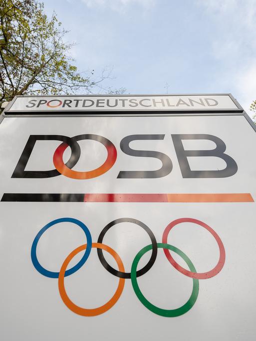 Das Logo "Deutscher Olympischer Sportbund" (DOSB) steht an dessen Hauptsitz auf einem Schild. Die Olympischen Ringe und  der Schriftzug "Sportdeutschland" sind auch abgebildet.