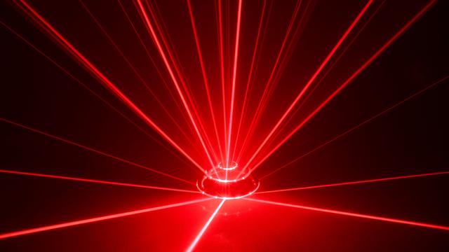 Rote Laserstrahlen leuchten vor schwarzem Hintergrund und ergeben in ihrer Bündelung den Anschein eines Alarmsignals.