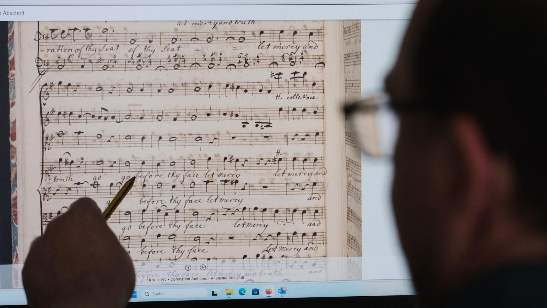 Ein Mann sitzt vor einen Computerbildschirm. Er zeigt mit einem Stift darauf. Zu sehen sind gescannte Partituren von Georg-Friedrich-Händel. 