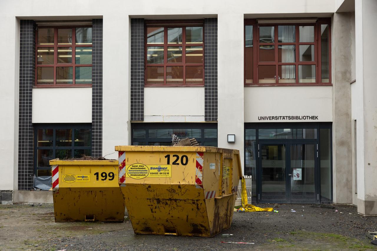 Bauabfall-Container stehen vor dem Eingang einer Universitätsbibliothek.