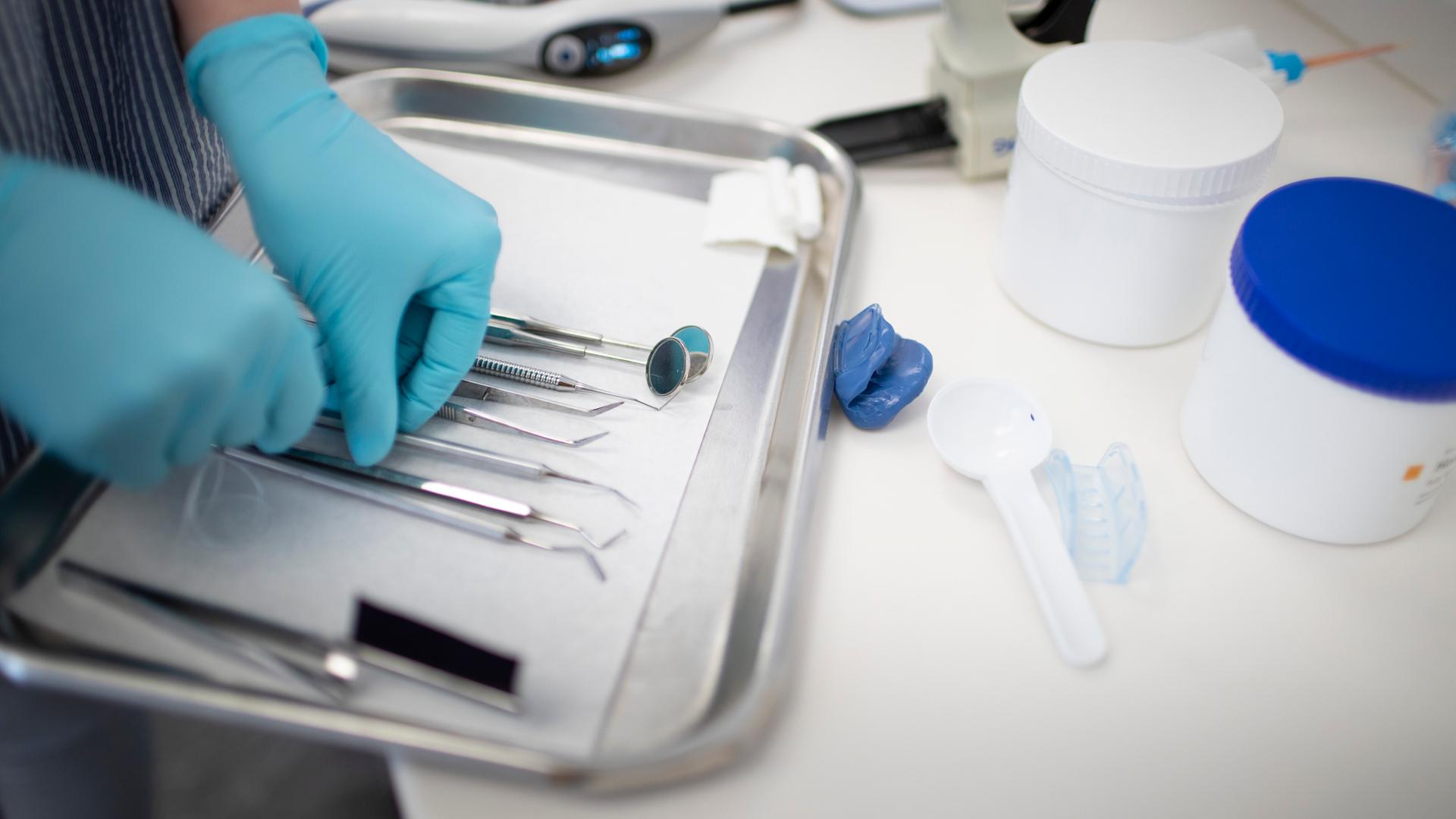 Beim Zahnarzt liegen Instrumentes eines Zahnmediziners auf dem Tablet, eine Person mit Handschuhen an den Händen ordnet die Geräte.
