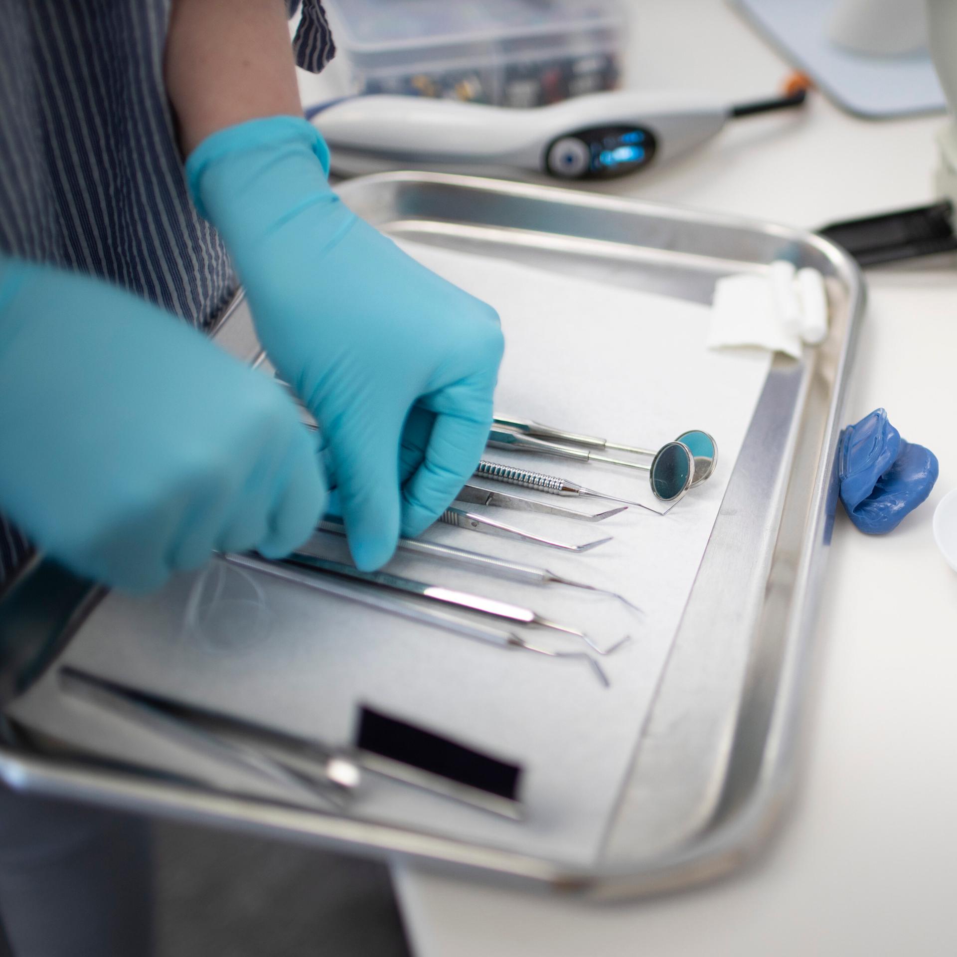 Beim Zahnarzt liegen Instrumentes eines Zahnmediziners auf dem Tablet, eine Person mit Handschuhen an den Händen ordnet die Geräte.