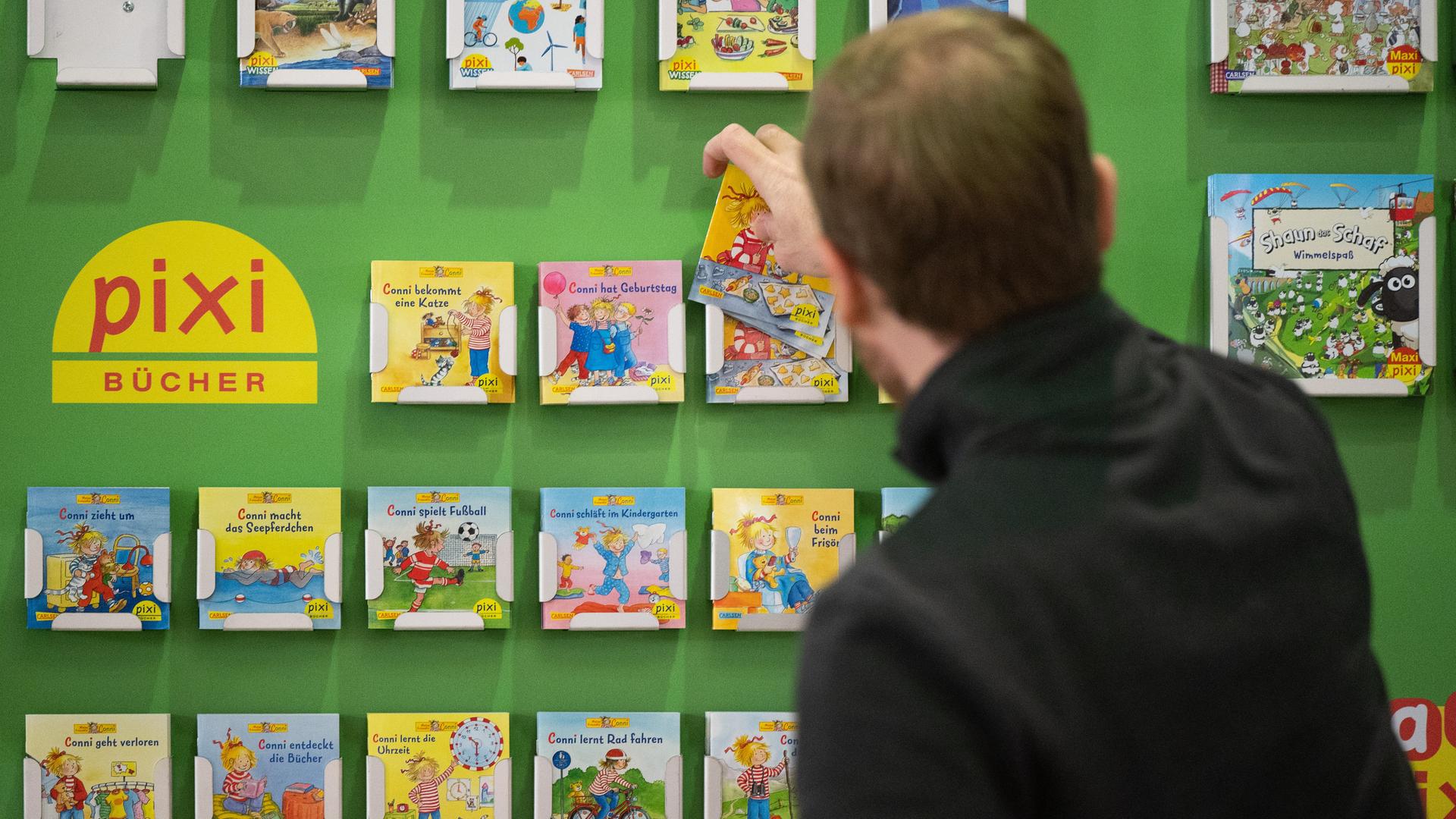 Ein Mann räumt am Stand des Carlsen Verlags Pixi-Kinderbücher in ein Regal. 