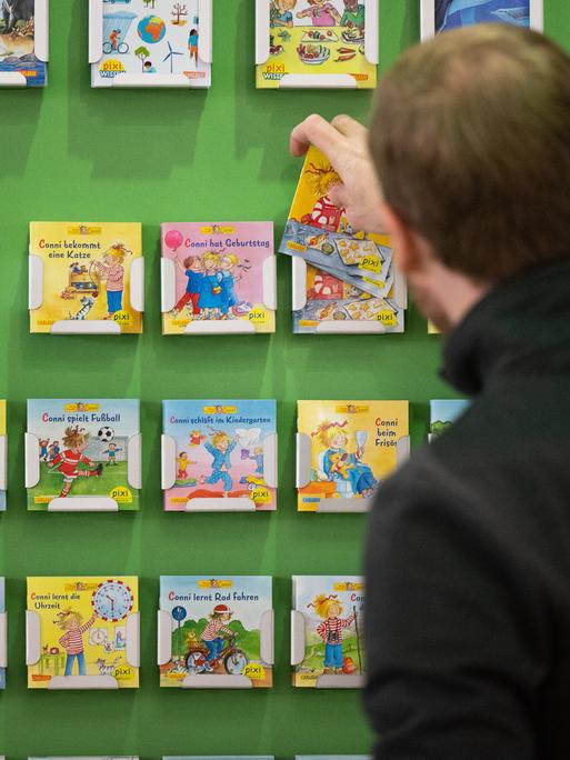 Ein Mann räumt am Stand des Carlsen Verlags Pixi-Kinderbücher in ein Regal. 