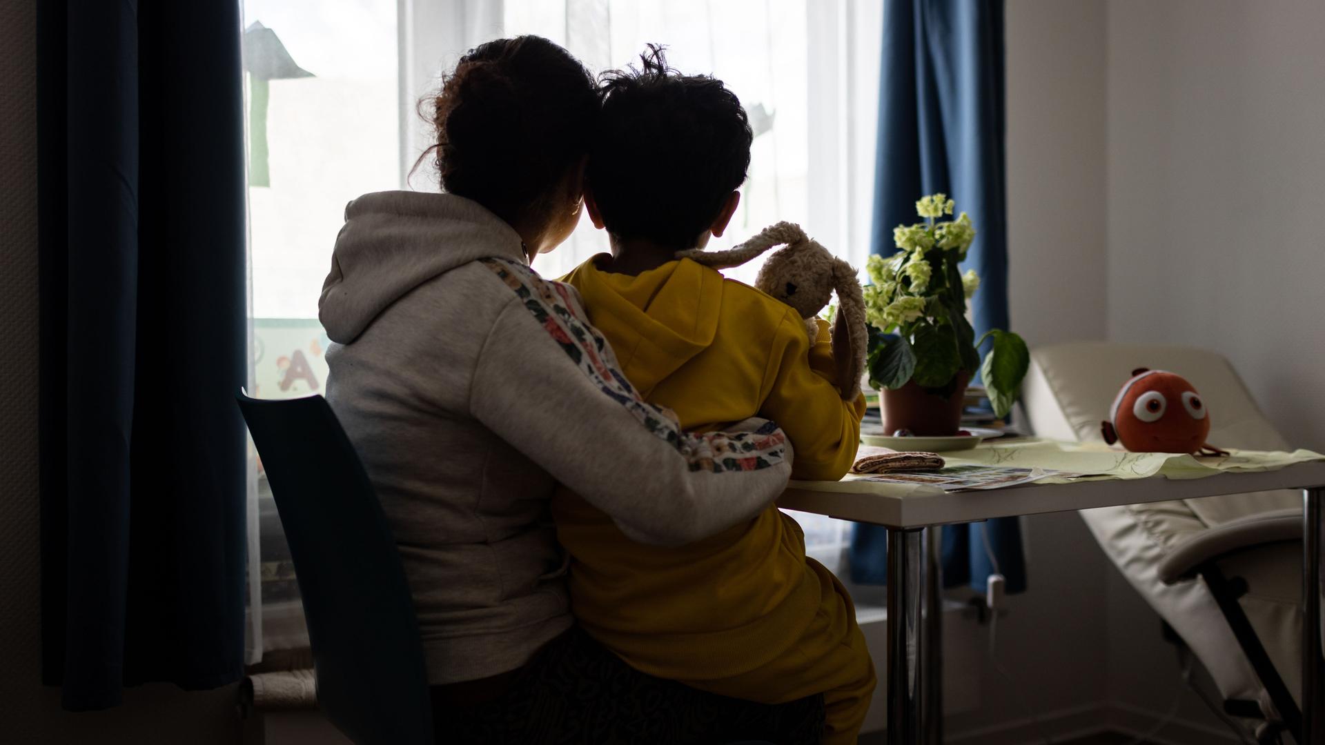 Eine Mutter und ein Kind sitzen im Frauenhaus der Caritas in Bochum vor einem Fenster und blicken nach draußen.