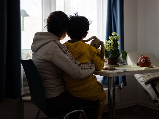 Eine Mutter und ein Kind sitzen im Frauenhaus der Caritas in Bochum vor einem Fenster und blicken nach draußen.