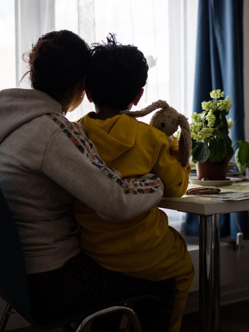 Eine Mutter und ein Kind sitzen im Frauenhaus der Caritas in Bochum vor einem Fenster und blicken nach draußen.