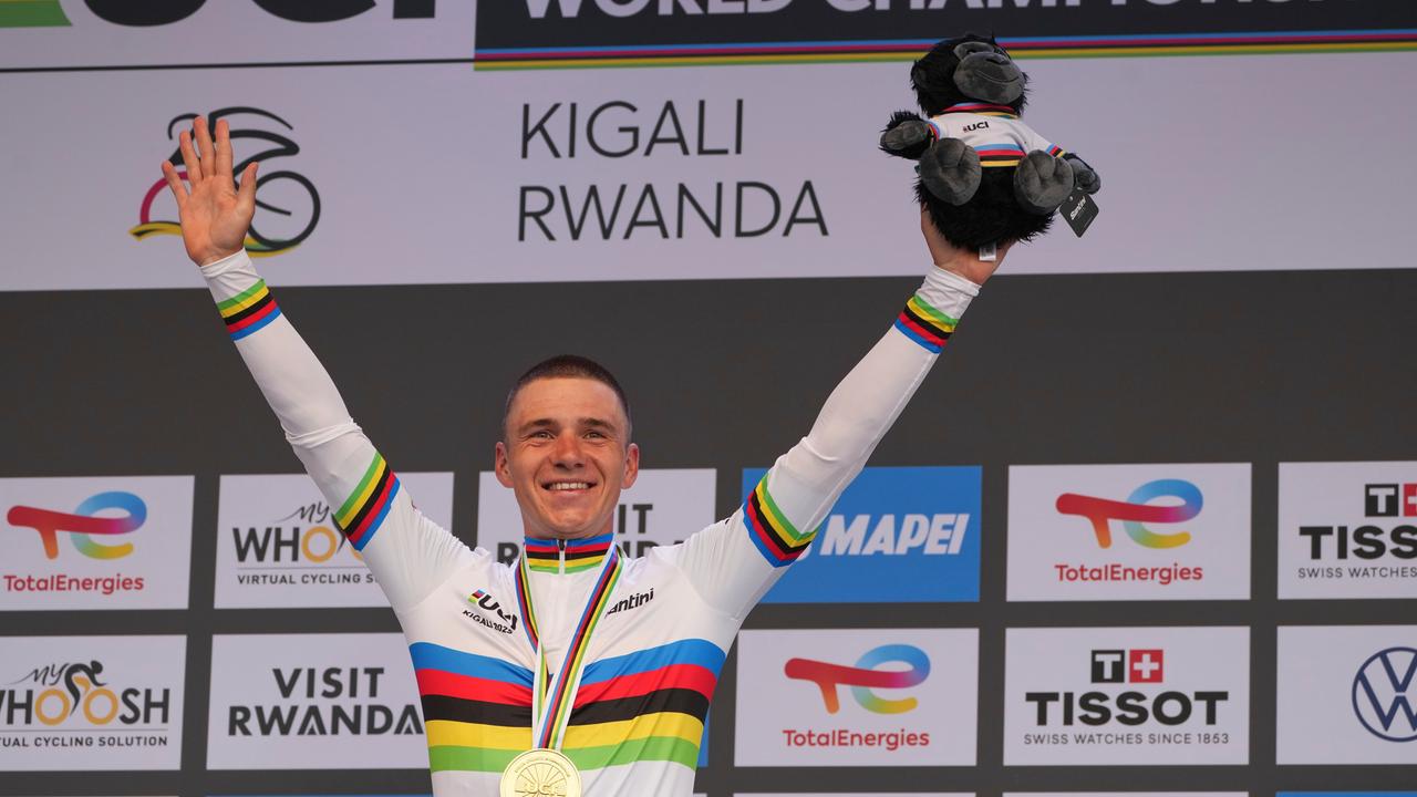 Der belgische Radprofi Remco Evenepoel hat eine Goldmedaille um den Hals, hält beide Arme in die Höhe und lächelt.