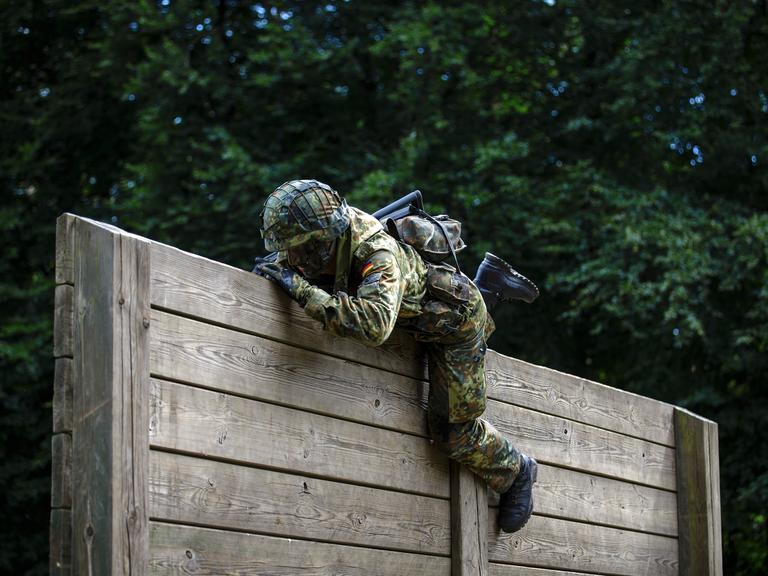 Ein Rekrut der Bundeswehr überwindet auf einem Hindernisparcours Holzlatten. 