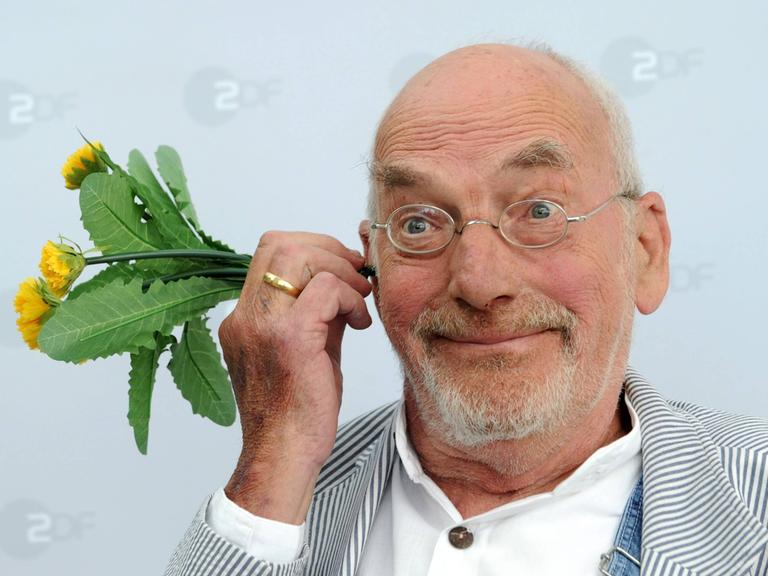 "Löwenzahn"-Moderator Peter Lustig hält sich eine Löwenzahn-Pflanze ans Ohr - bei einem Foto-Shooting anlässlich des 30-jährigen Jubiläums der ZDF-Sendung "Löwenzahn" im Jahr 2010.