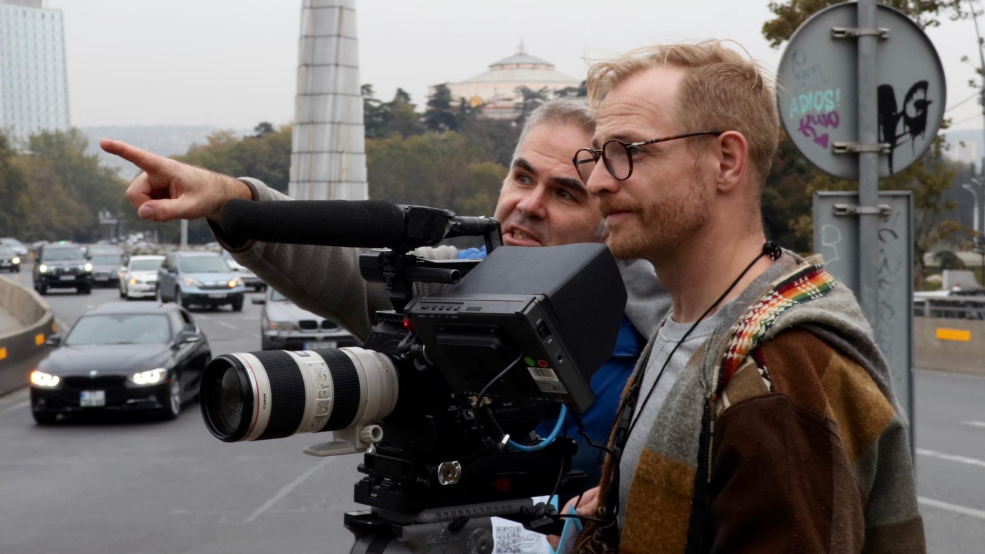 Zwei Männer stehen mit einer Kamera auf einer Straßenkreuzung und diskutieren.