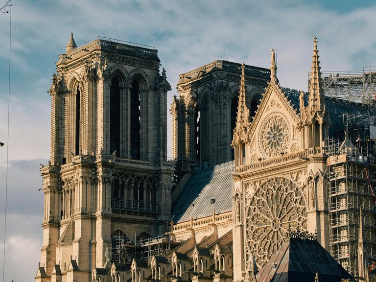 Außenansicht von Notre-Dame: Die Kathedrale hat beeindruckende Fenster, viele Verzierungen an der Fassade und Türme.