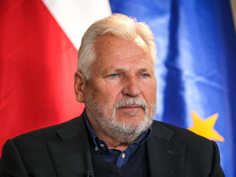 Der frühere polnische Präsident Aleksander Kwasniewski mit weißem Bart vor der polnischen und der EU-Fahne. 
