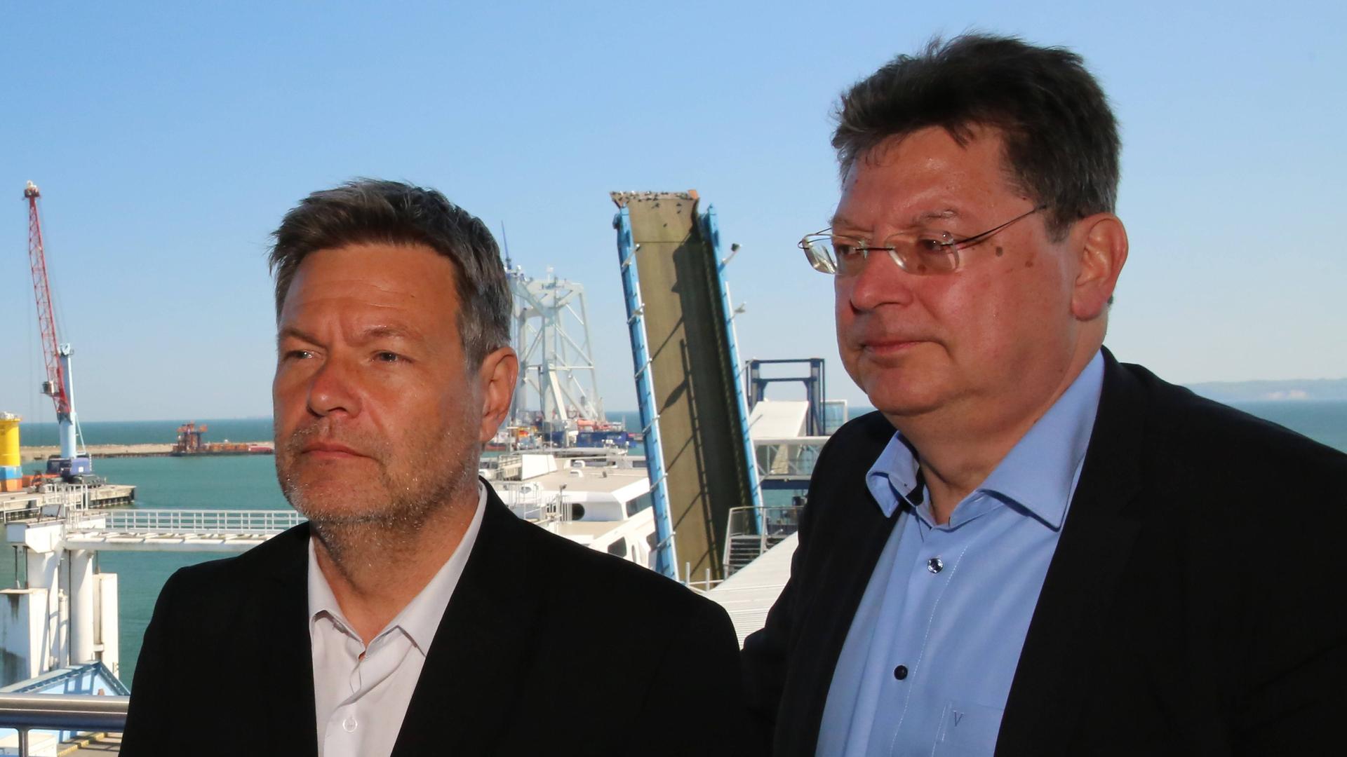 Bundeswirschaftsminister Habeck (l.) steht mit seinem Amtskollegen Meyer aus Mecklenburg-Vorpommern auf der Insel Rügen im Gebäude des Fährhafens Sassnitz Mukran. Im Hintergrund sieht man ein Schiff und eine hochgezogene Brücke. Bundeswirschaftsminister Habeck (l.) steht mit seinem Amtskollegen Meyer aus Mecklenburg-Vorpommern auf der Insel Rügen im Gebäude des Fährhafens Sassnitz Mukran. Im Hintergrund sieht man ein Schiff und eine hochgezogene Brücke.