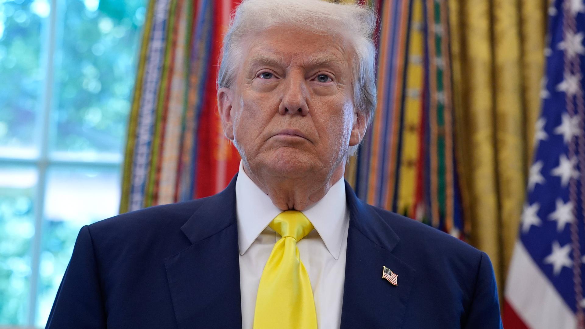 US-Präsident Donald Trump steht vor den Fahnen im Oval Office des Weißen Hauses in Washington und schaut mit ernstem Gesichtsausdruck US-Präsident Donald Trump steht vor den Fahnen im Oval Office des Weißen Hauses in Washington und schaut mit ernstem Gesichtsausdruck