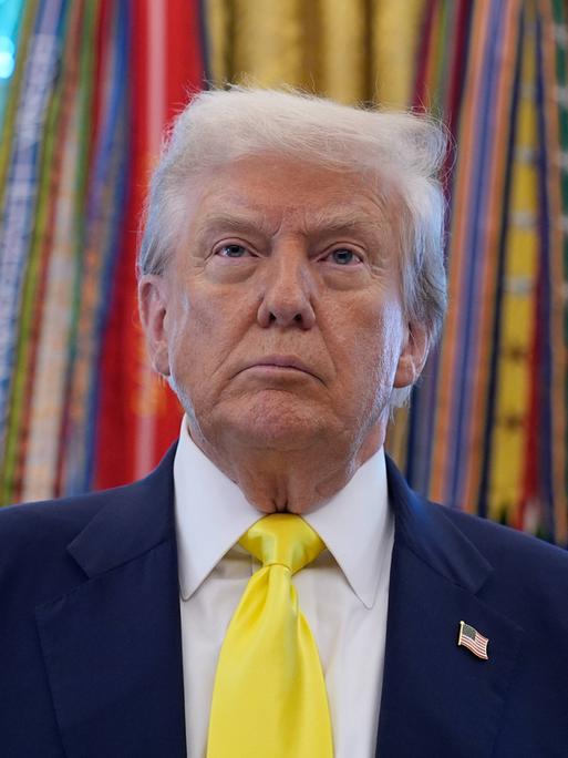 US-Präsident Donald Trump steht vor den Fahnen im Oval Office des Weißen Hauses in Washington und schaut mit ernstem Gesichtsausdruck