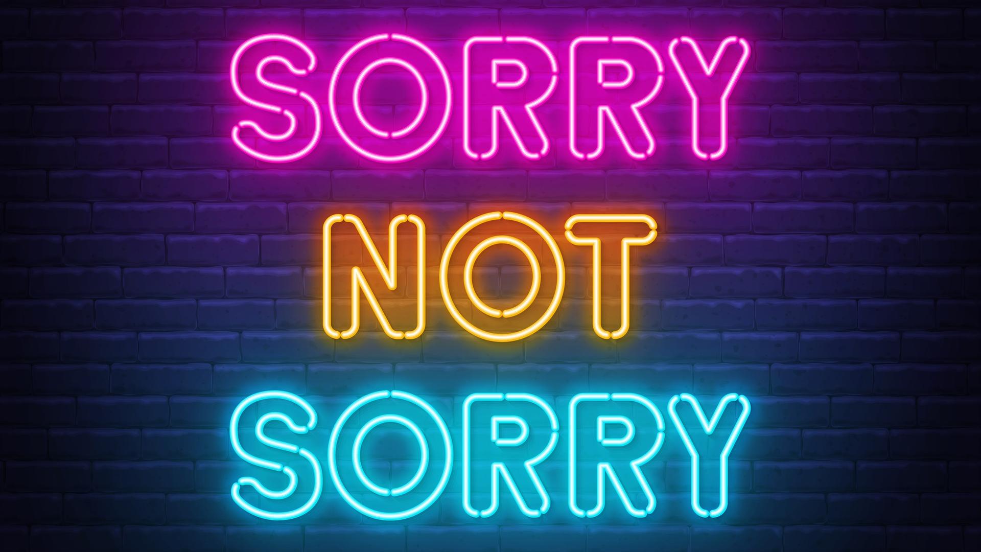 "Sorry not Sorry" Neonbuchstaben vor einer dunklen Ziegelmauer "Sorry not Sorry" Neonbuchstaben vor einer dunklen Ziegelmauer