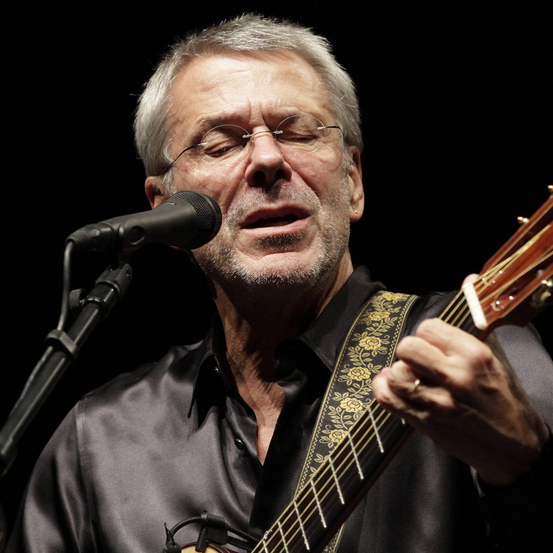 Reinhard Mey steht am Mikro und singt mit der Gitarre in der Hand. 