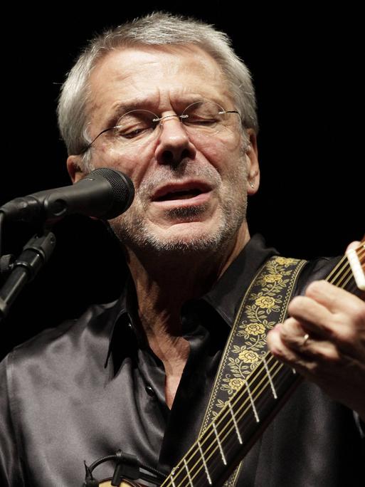 Reinhard Mey steht am Mikro und singt mit der Gitarre in der Hand. 