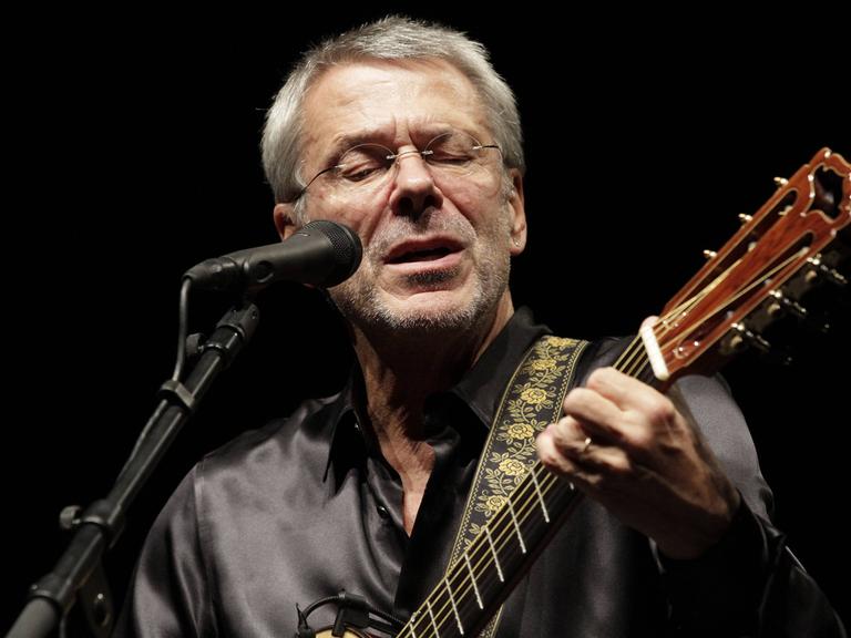 Reinhard Mey steht am Mikro und singt mit der Gitarre in der Hand. 