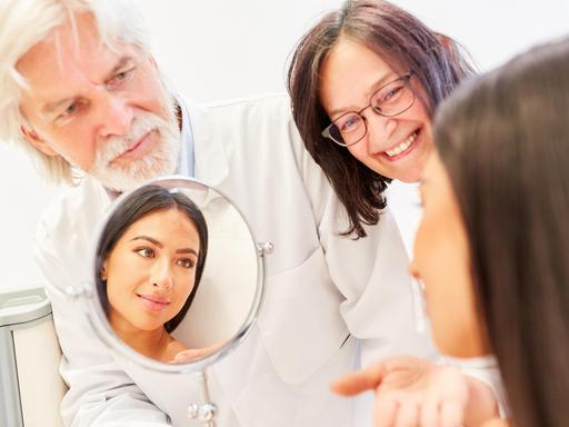 Ãrzteteam der Schönheitsklinik mit Spiegel im Beratungsgespräch mit einer Patientin || Modellfreigabe vorhanden Ãrzteteam der Schönheitsklinik mit Spiegel im Beratungsgespräch mit einer Patientin || Modellfreigabe vorhanden