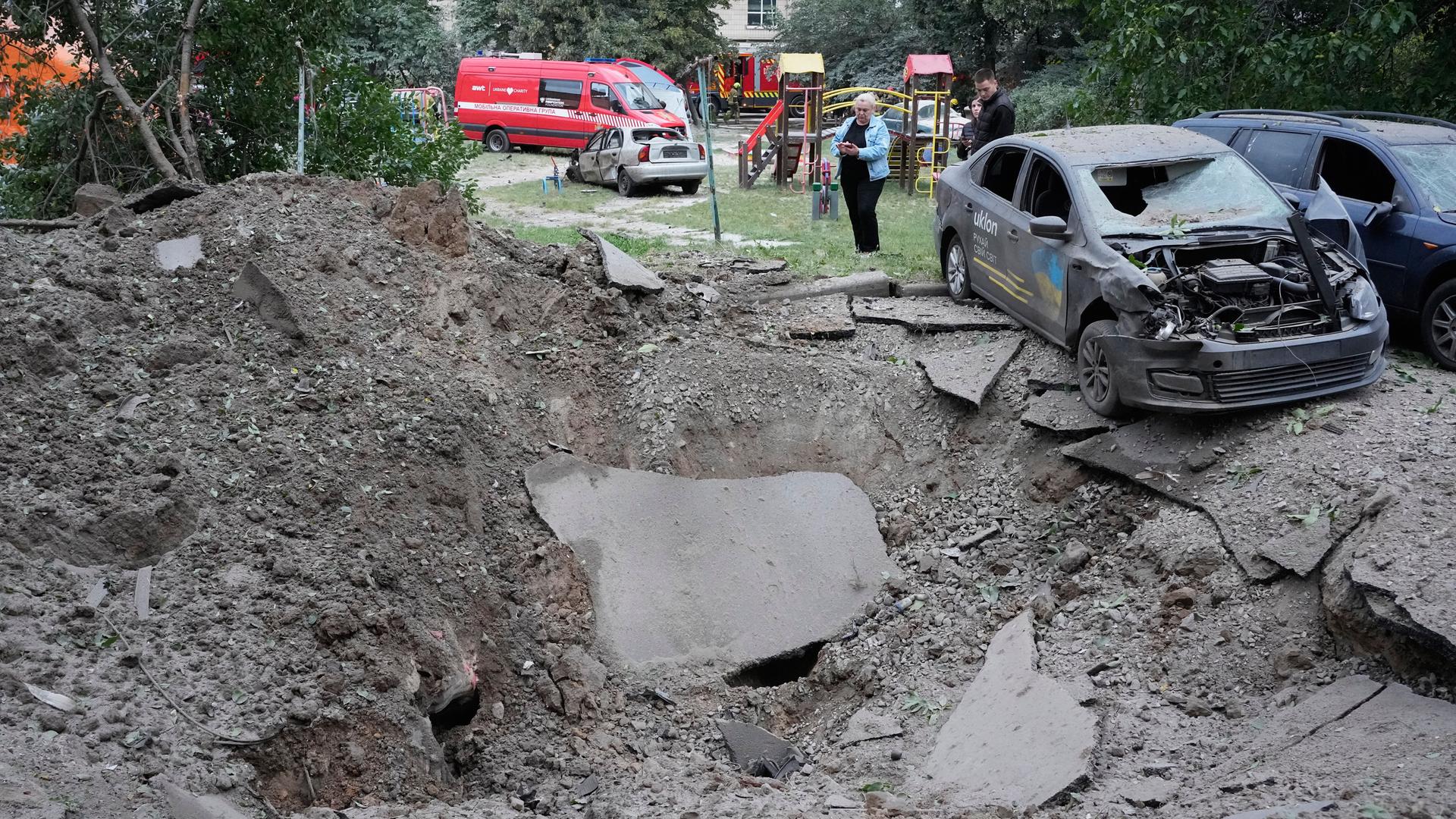 Anwohner stehen in Kiew neben einem Krater und durch einen russischen Raketenangriff beschädigten Autos. Anwohner stehen in Kiew neben einem Krater und durch einen russischen Raketenangriff beschädigten Autos.