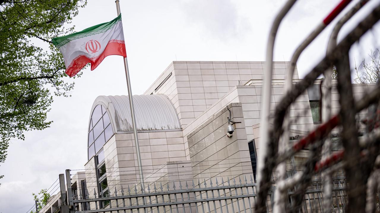 Absperrgitter stehen vor der iranischen Botschaft in Berlin. Über dem Gebäude weht eine iranische Flagge. 