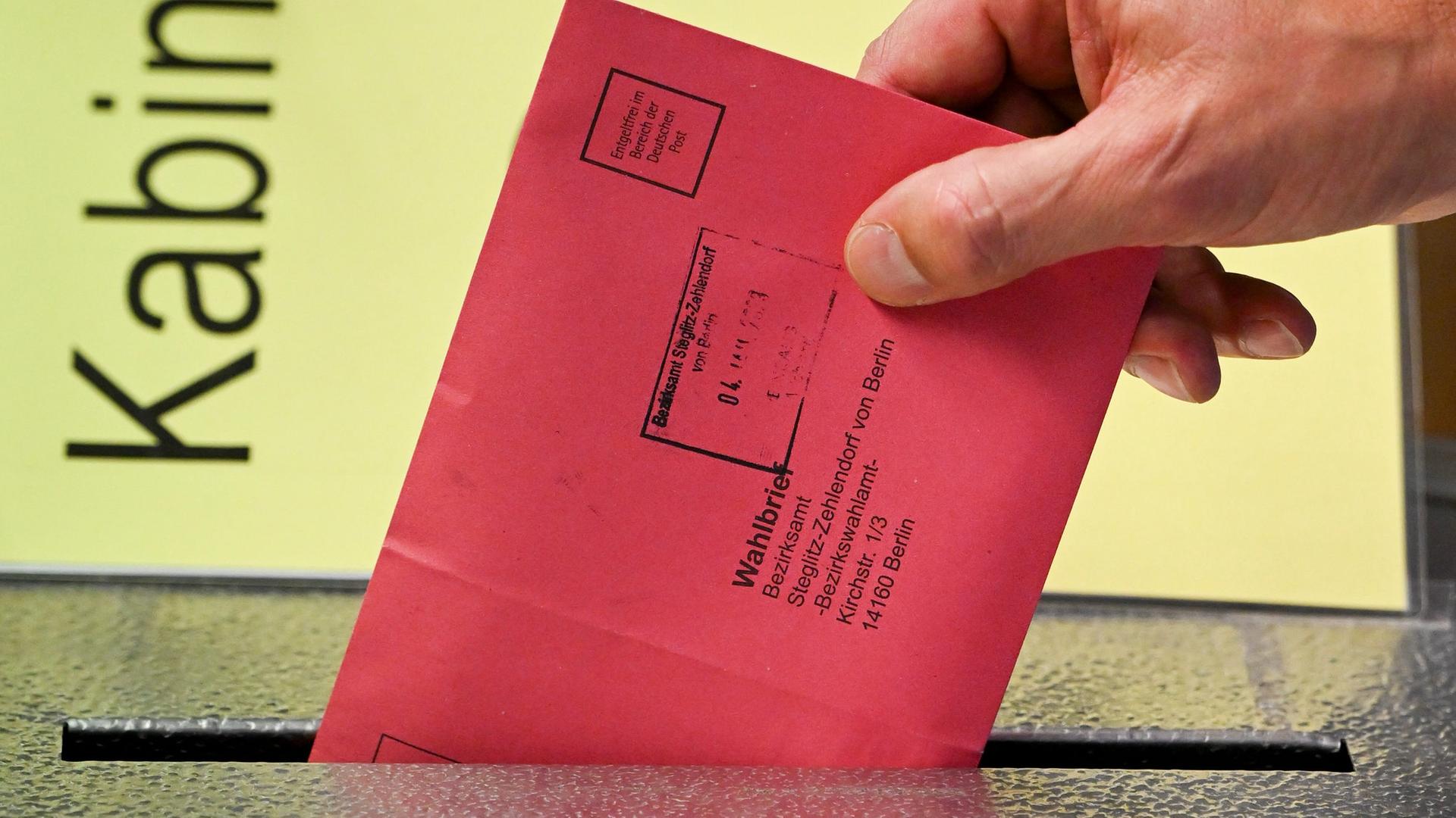Zum Beginn der Briefwahl für die Wiederholungswahlen am 12. Februar zum Abgeordnetenhaus in Berlin wählt eine Person vorab und steckt Stimmzettel in einem roten Briefumschlag für die Briefwahl in die Wahlurne. Zu sehen ist nur seine Hand.