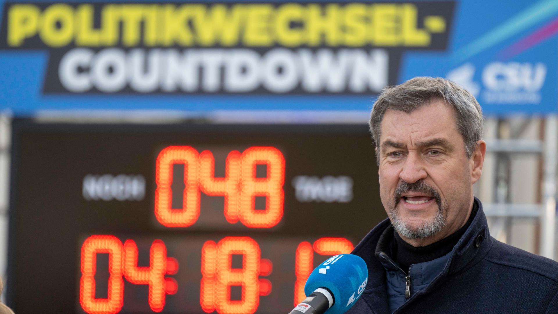 Der CSU-Parteivorsitzende Markus Söder steht im Freien mit geöffnetem Mund vor einem Mikrofon. Im Hintergrund ist ein Digitalbanner mit dem Schriftzug "Politikwechsel Countdown" zu sehen und eine Uhr, die  die Zeit bis zur Bundestagswahl zeigt.