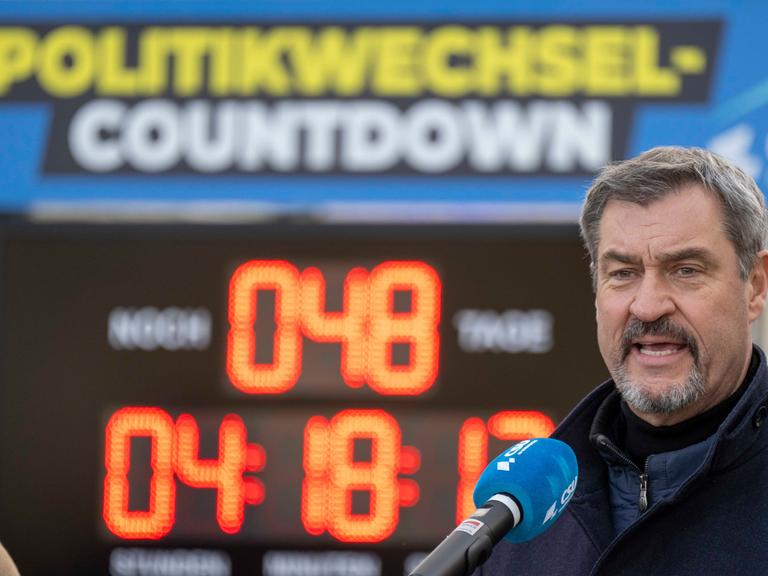 Der CSU-Parteivorsitzende Markus Söder steht im Freien mit geöffnetem Mund vor einem Mikrofon. Im Hintergrund ist ein Digitalbanner mit dem Schriftzug "Politikwechsel Countdown" zu sehen und eine Uhr, die  die Zeit bis zur Bundestagswahl zeigt.