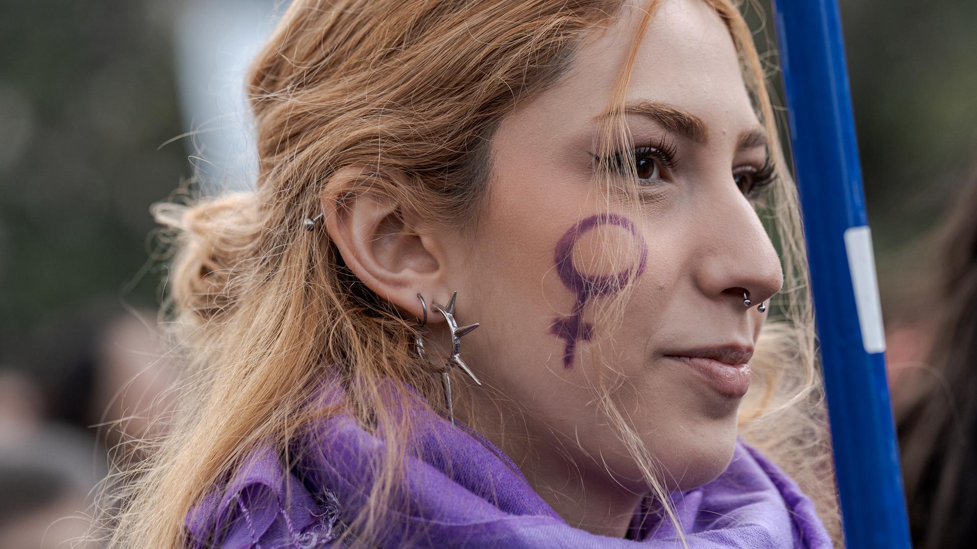 Eine Frau trägt das Symbol des weiblichen Geschlechts auf der Wange. Eine Frau trägt das Symbol des weiblichen Geschlechts auf der Wange.