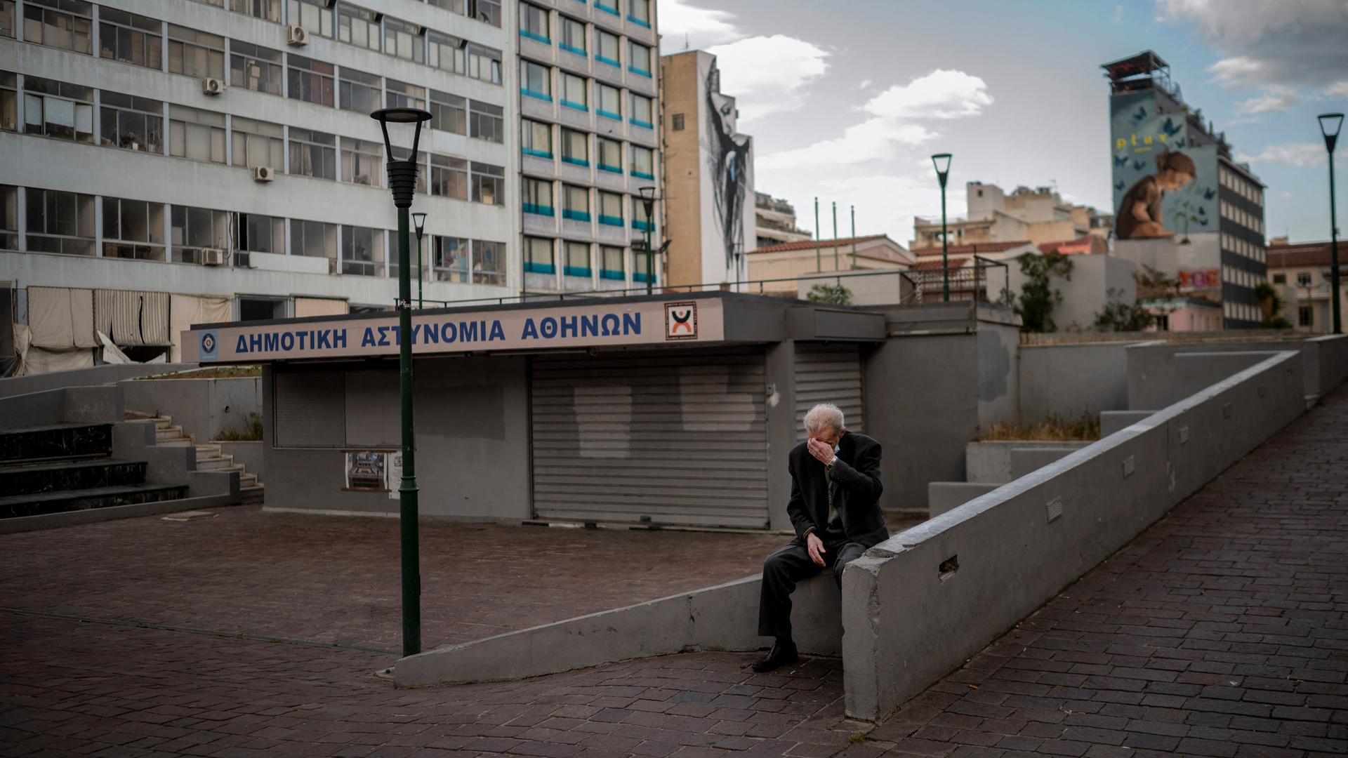 Ein älterer Mann sitzt auf einem verlassenen Marktplatz in Athen.