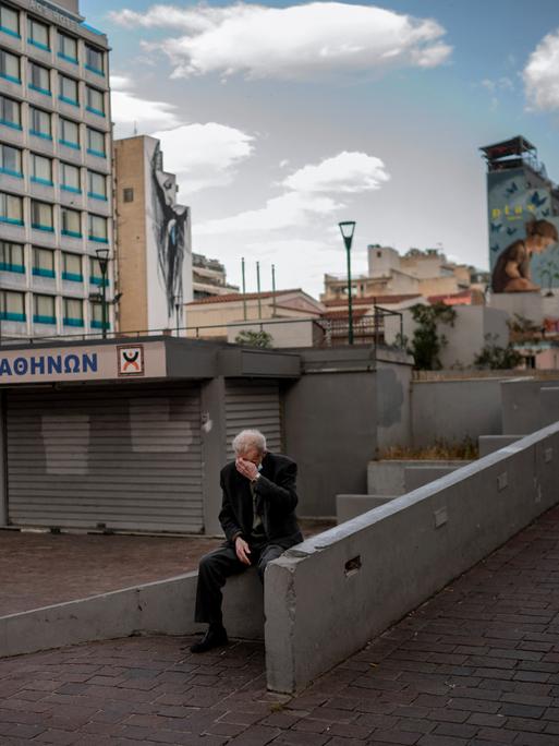 Ein älterer Mann sitzt auf einem verlassenen Marktplatz in Athen.