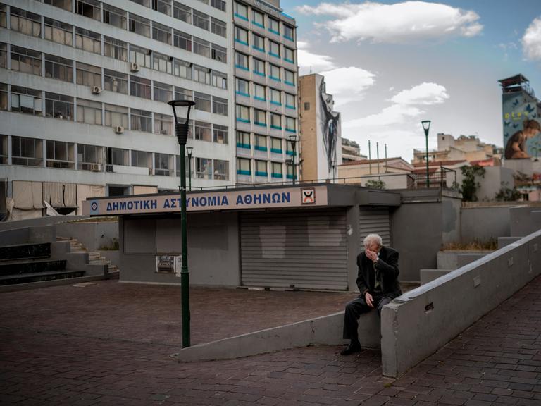 Ein älterer Mann sitzt auf einem verlassenen Marktplatz in Athen.
