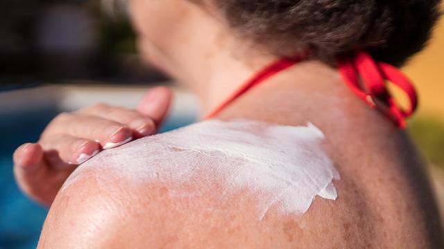 Eine Frau im Bikini cremt sich ihre Schulter mit Sonnenmilch ein. 