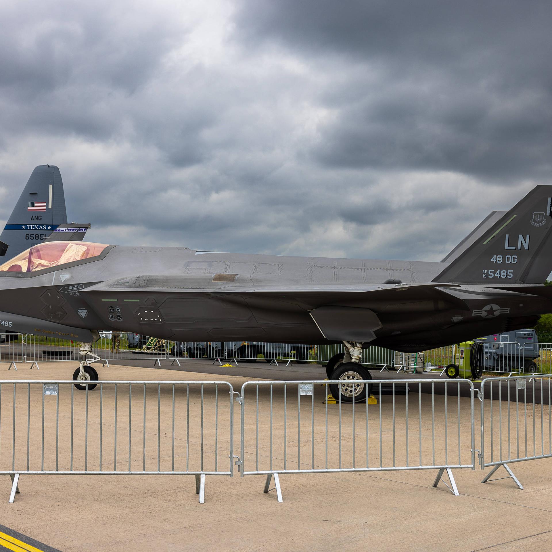 Ein Lockheed Martin F-35A Lightning II der U.S. Air Force 48th Operations Group ist auf einem Freigelände als statisches Ausstellungsstück zu sehen. Im Hintergrund ist das Leitwerk eines weiteren Militärflugzeugs mit der Aufschrift Texas ANG erkennbar. 