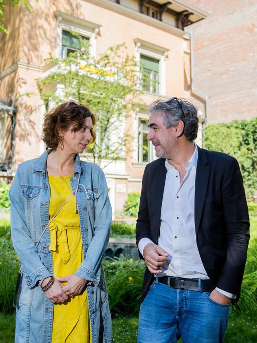 Eva Menasse und Deniz Yücel stehen im Garten des Literaturhauses Berlin und lächeln sich an.