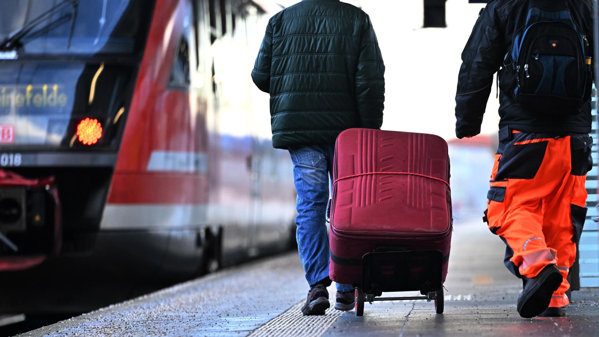 Eine Regionalbahn steht zur Abfahrt bereit im Erfurter Hauptbahnhof. Daneben laufen ein Fahrgast mit einem roten Koffer und ein Bahnmitarbeiter in orangener Arbeitskleidung. Eine Regionalbahn steht zur Abfahrt bereit im Erfurter Hauptbahnhof. Daneben laufen ein Fahrgast mit einem roten Koffer und ein Bahnmitarbeiter in orangener Arbeitskleidung.