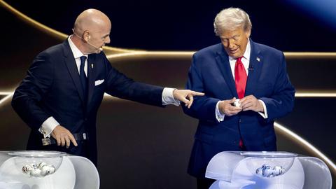 Gianni Infantino und Donald Trump stehen auf einer Bühne vor zwei Lostöpfen. Trump ist dabei, ein Los zu öffnen. Infantino zeigt auf ihn.