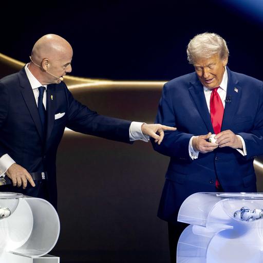 Gianni Infantino und Donald Trump stehen auf einer Bühne vor zwei Lostöpfen. Trump ist dabei, ein Los zu öffnen. Infantino zeigt auf ihn.