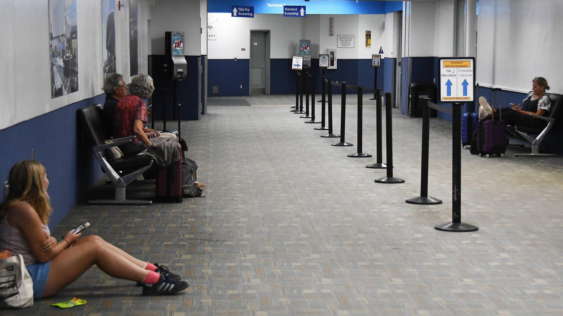 Menschen an einem Flughafen sitzen auf Bänken oder am Boden und warten. 