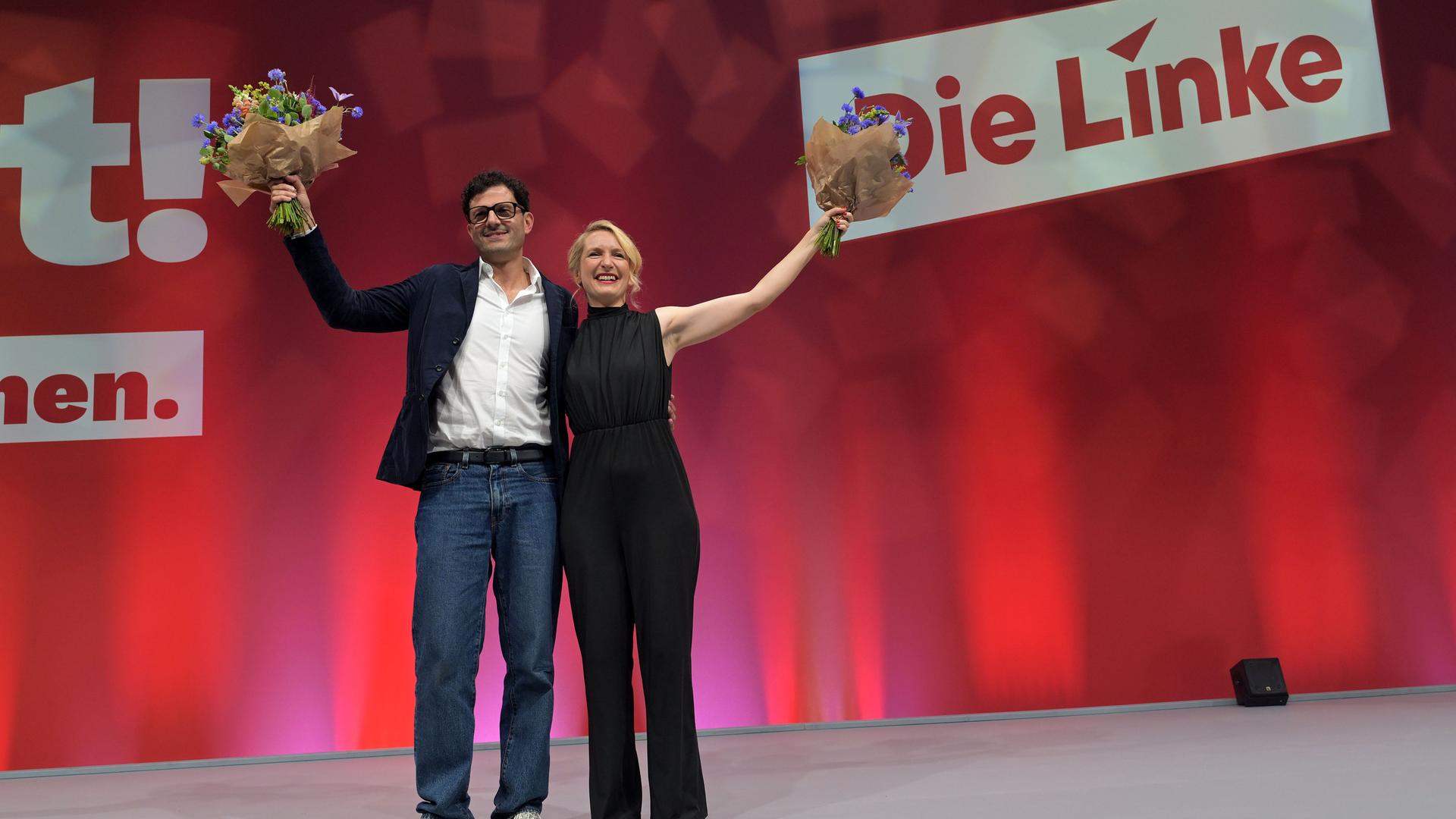 Luigi Pantisano und Ines Schwerdtner sind die neue Doppelspitze der Partei Die Linke. Sie stehen nach ihrer Wahl auf einer Bühne und halten Blumensträuße in den Händen. Luigi Pantisano und Ines Schwerdtner sind die neue Doppelspitze der Partei Die Linke. Sie stehen nach ihrer Wahl auf einer Bühne und halten Blumensträuße in den Händen.