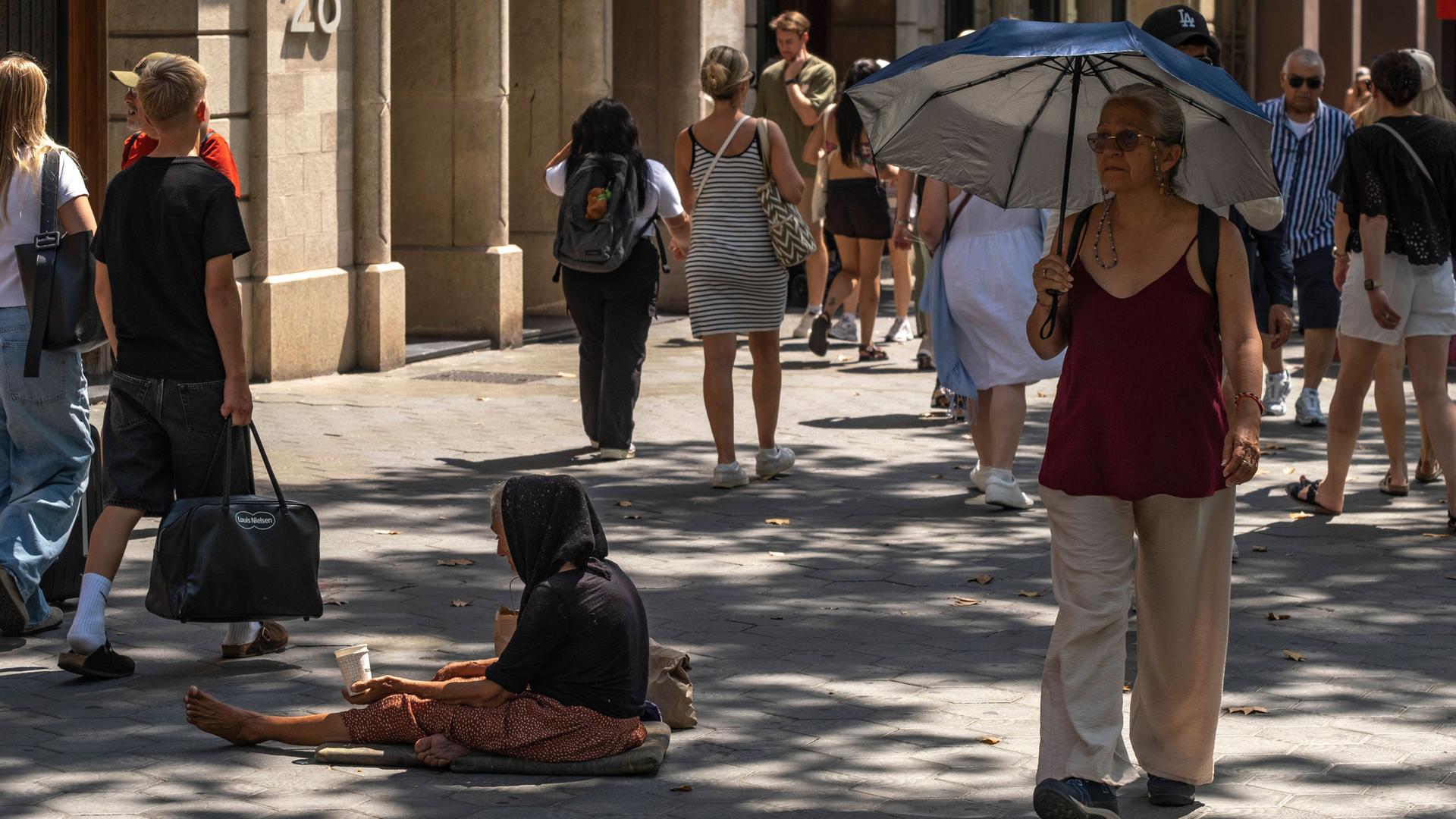 Das Foto zeigt Menschen auf einer Straße in Barcelona, darunter auch eine Bettlerin. Die Menschen leiden unter den sehr hohen Temperaturen. ZUMAs197 20250815_aab_s197_038 Copyright: xPacoxFreirex