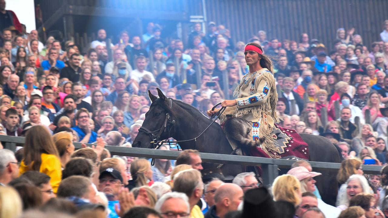 Ein Mann auf einen Pferd mit Federschmuck reitet durch eine Menschenmenge.